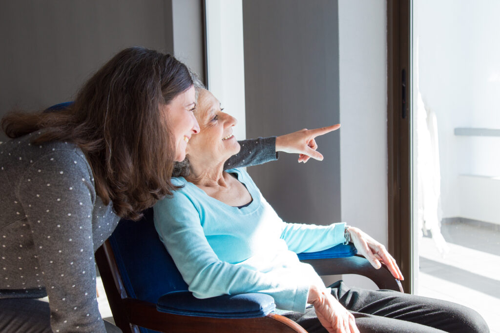 A smiling elderly woman and her care provider together enjoying a scenic view, symbolizing care and connection in a caregiving context.