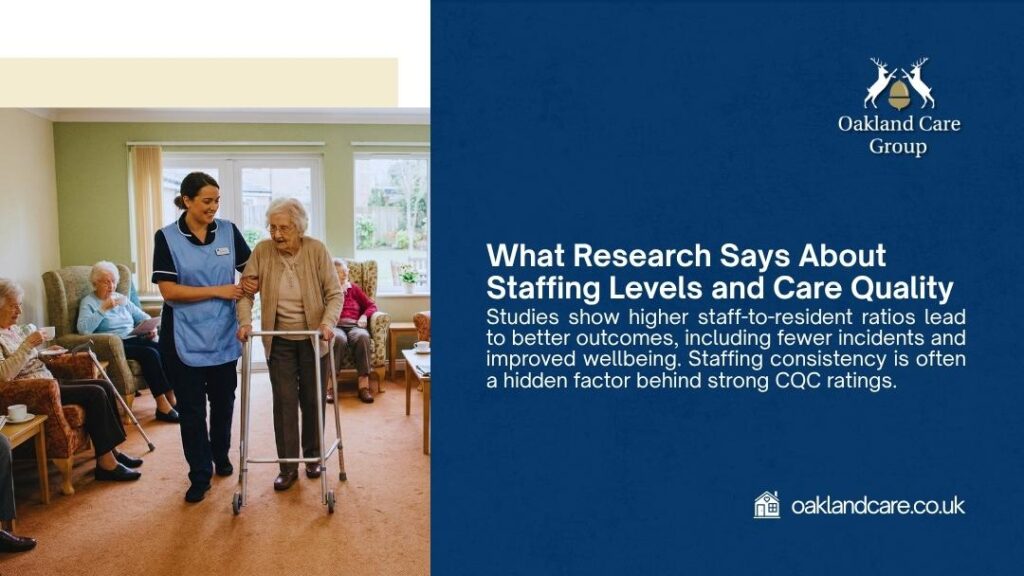 Smiling care worker in blue uniform gently assisting an elderly woman with a walking frame in a bright care home lounge, with other residents seated in the background.